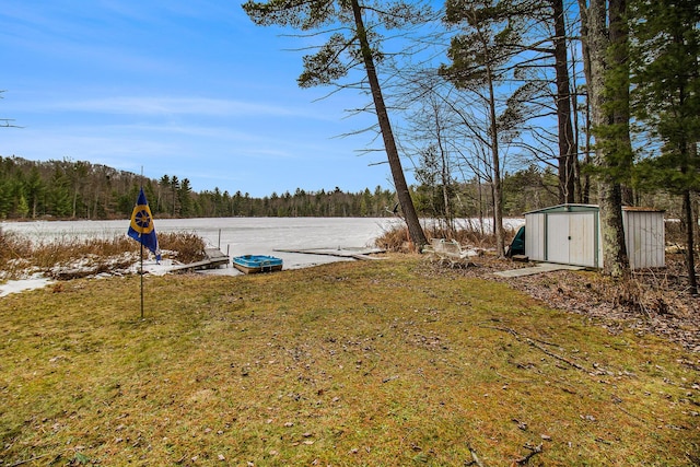 view of yard with a storage unit, a water view, an outbuilding, and a forest view