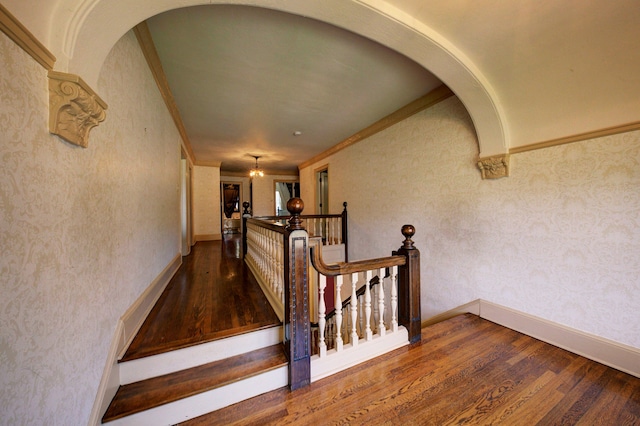 stairway with arched walkways, wood finished floors, and ornamental molding