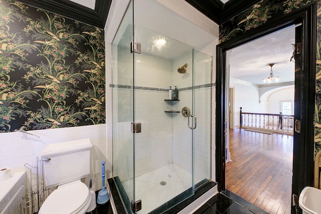 full bathroom with crown molding, a stall shower, a wainscoted wall, toilet, and wallpapered walls