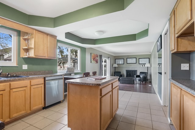 kitchen featuring a brick fireplace, light brown cabinetry, dishwasher, and a kitchen island