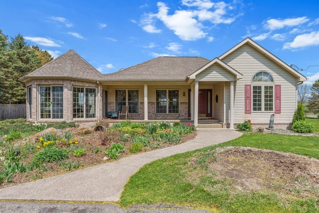ranch-style house featuring a porch, brick siding, fence, and roof with shingles