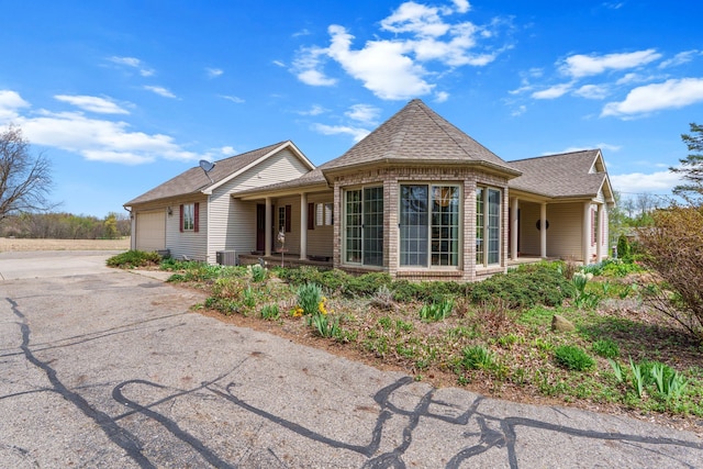 exterior space with a garage, covered porch, central AC unit, a shingled roof, and driveway