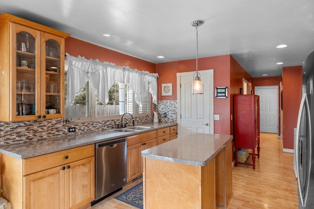 kitchen with appliances with stainless steel finishes, a sink, light wood-style flooring, a center island, and decorative backsplash