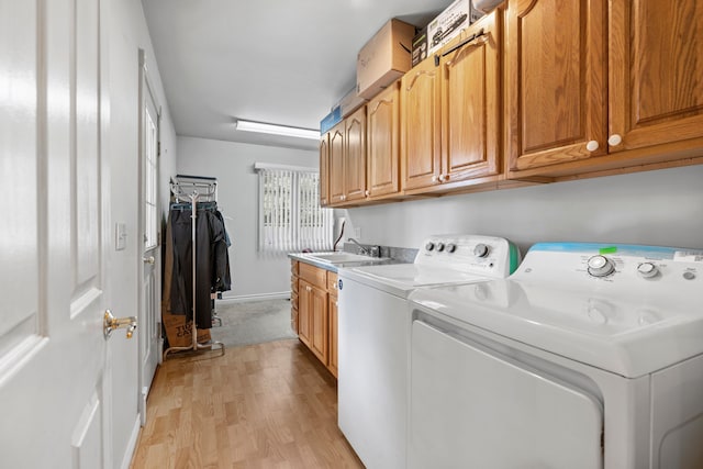 washroom with washing machine and clothes dryer, cabinet space, a sink, baseboards, and light wood-style floors