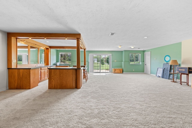 unfurnished living room with baseboards, a textured ceiling, visible vents, and light carpet
