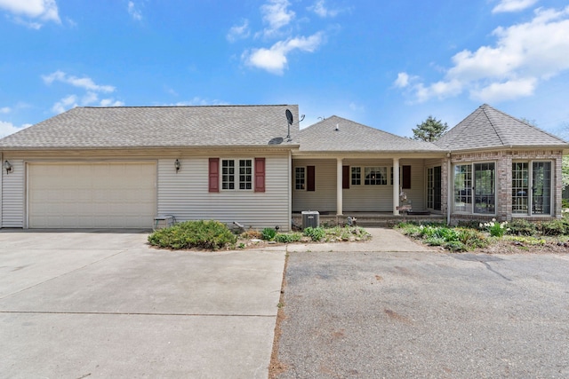 ranch-style house with roof with shingles, a garage, central AC unit, covered porch, and driveway