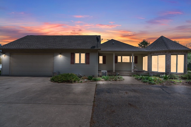 view of front facade with covered porch, driveway, a shingled roof, and a garage
