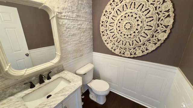 bathroom with toilet, a wainscoted wall, a decorative wall, and vanity