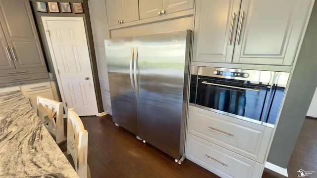 kitchen featuring light stone countertops, white cabinets, stainless steel appliances, and dark wood-type flooring