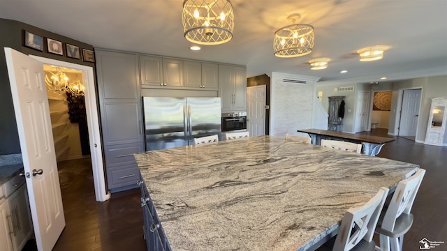 kitchen with light stone countertops, an inviting chandelier, appliances with stainless steel finishes, dark wood-style flooring, and visible vents