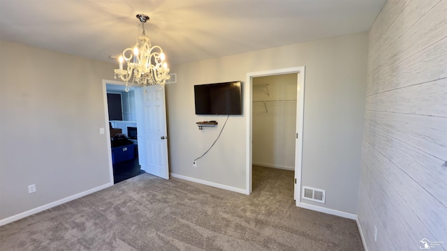 unfurnished bedroom featuring a chandelier, carpet, wood walls, a walk in closet, and visible vents