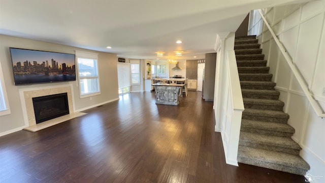 living room featuring a glass covered fireplace, stairway, dark wood-type flooring, and recessed lighting