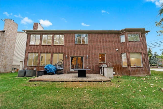 back of property with a lawn, brick siding, a chimney, and a patio