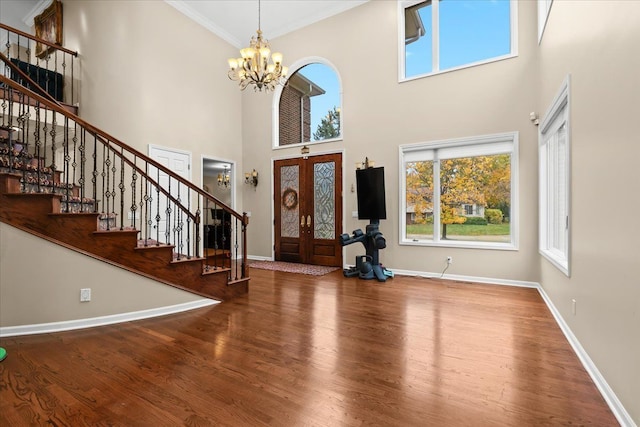 entrance foyer with crown molding, a towering ceiling, wood finished floors, baseboards, and a notable chandelier