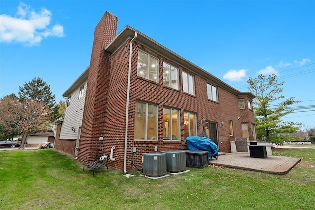 rear view of property featuring cooling unit, a chimney, a yard, and brick siding