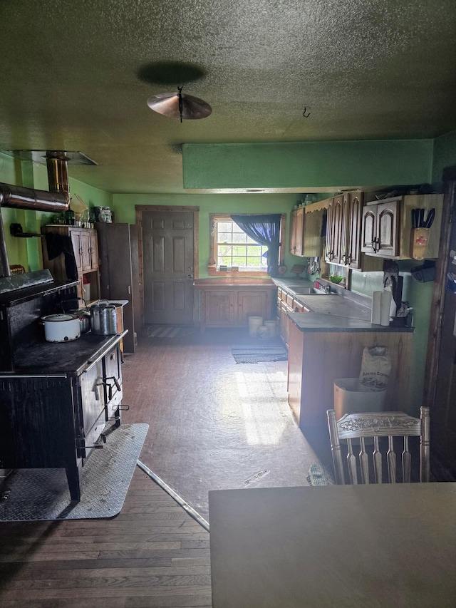 kitchen featuring wood finished floors, a peninsula, freestanding refrigerator, and a wood stove