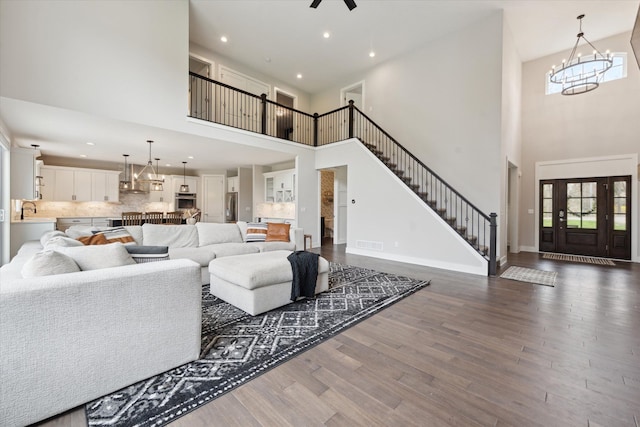 living area with dark wood-style flooring, stairs, recessed lighting, baseboards, and a towering ceiling