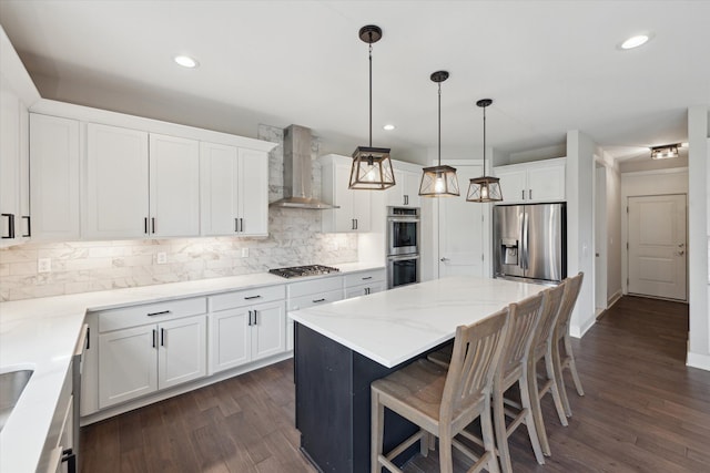 kitchen featuring wall chimney exhaust hood, appliances with stainless steel finishes, a kitchen island, and dark wood-style floors