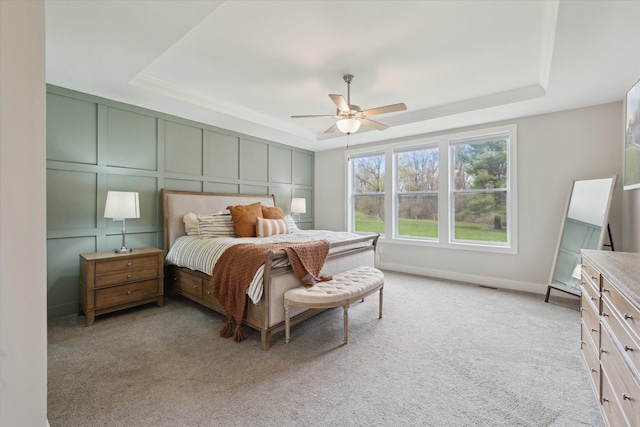 bedroom with light colored carpet, a raised ceiling, and a decorative wall