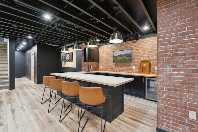bar featuring beverage cooler, pendant lighting, light wood finished floors, and stairs