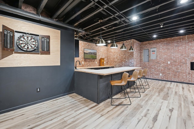 bar with wood finished floors, brick wall, indoor wet bar, baseboards, and electric panel