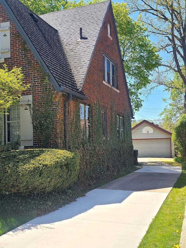view of side of property with a detached garage, brick siding, an outbuilding, and roof with shingles