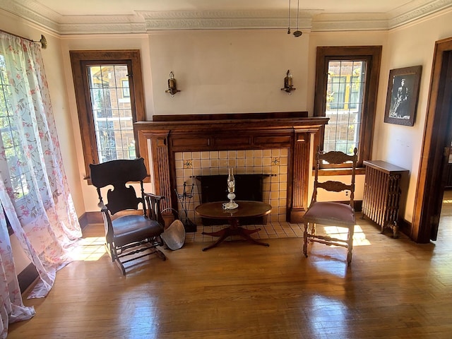 sitting room featuring a fireplace, wood-type flooring, radiator heating unit, baseboards, and ornamental molding