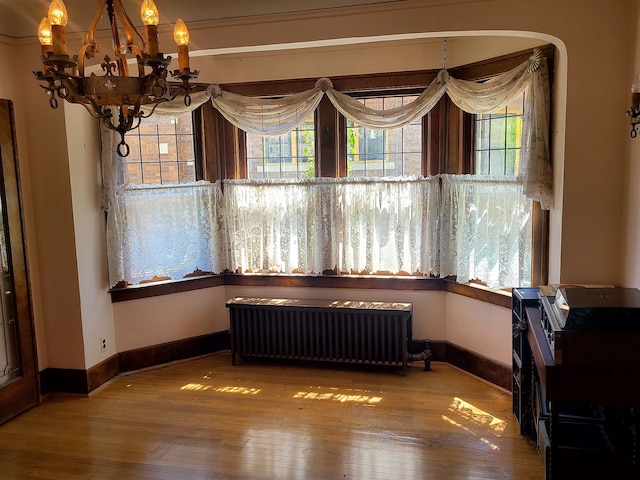 dining space featuring a chandelier, hardwood / wood-style floors, baseboards, and radiator