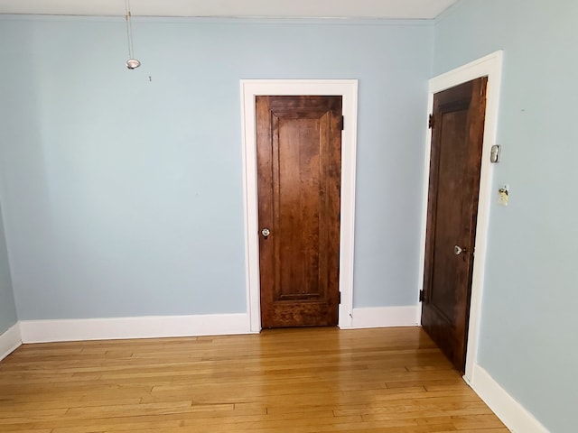 empty room featuring crown molding, light wood finished floors, and baseboards