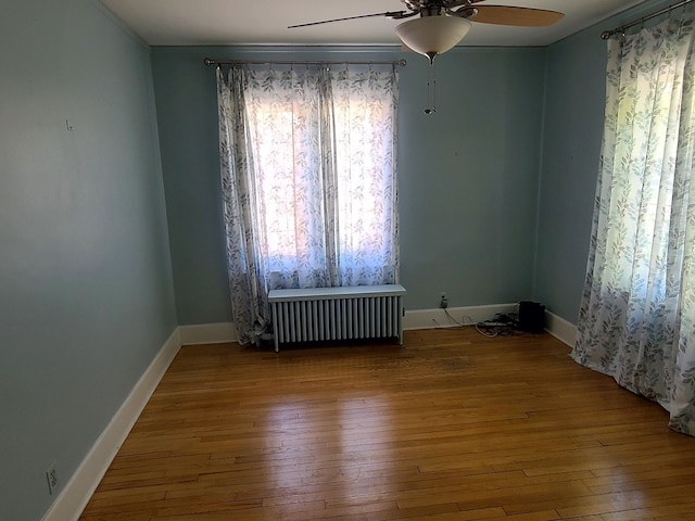 empty room featuring radiator, ceiling fan, hardwood / wood-style floors, and baseboards