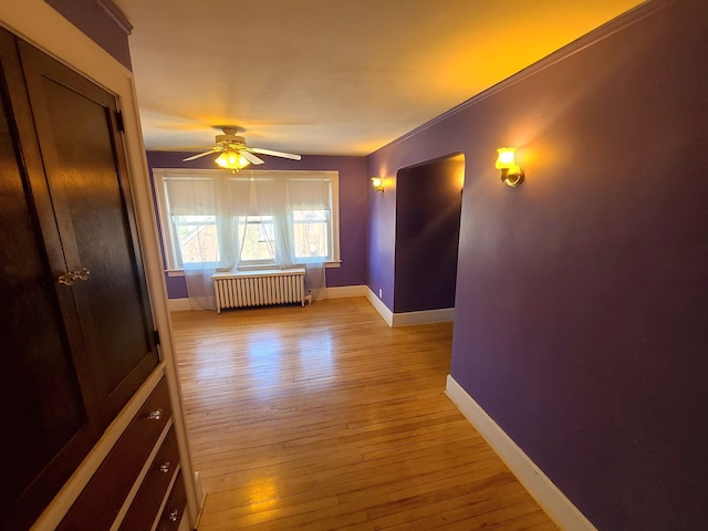 unfurnished room featuring radiator heating unit, light wood-style floors, a ceiling fan, and baseboards