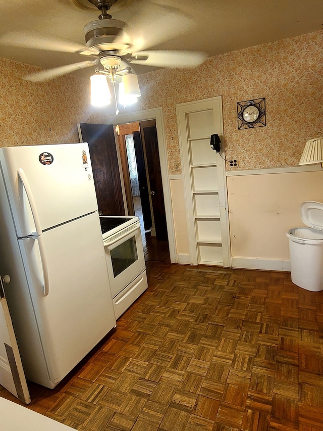 kitchen with ceiling fan, white appliances, a wainscoted wall, and wallpapered walls