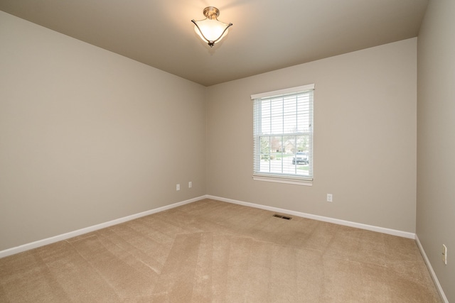 empty room featuring baseboards, visible vents, and light carpet