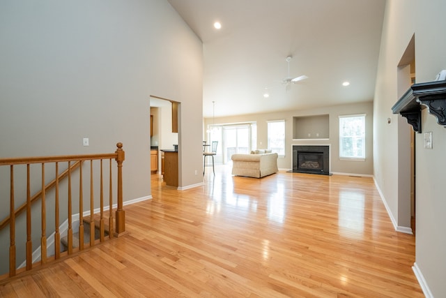 unfurnished living room with a glass covered fireplace, high vaulted ceiling, a ceiling fan, and light wood-style flooring