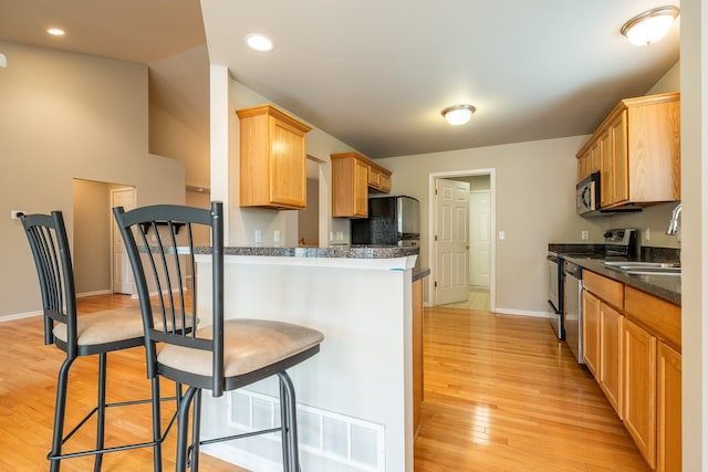 kitchen with a kitchen breakfast bar, a sink, baseboards, light wood-style floors, and stainless steel appliances