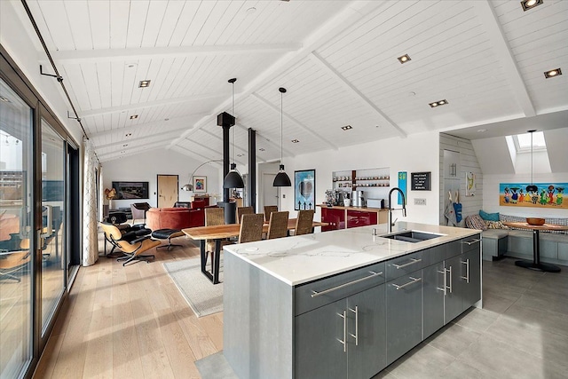 kitchen with a sink, gray cabinets, open floor plan, vaulted ceiling with beams, and a center island with sink