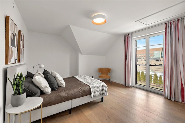 bedroom featuring light wood-style floors, access to exterior, attic access, baseboards, and lofted ceiling