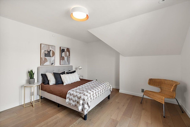 bedroom with baseboards, wood finished floors, and lofted ceiling