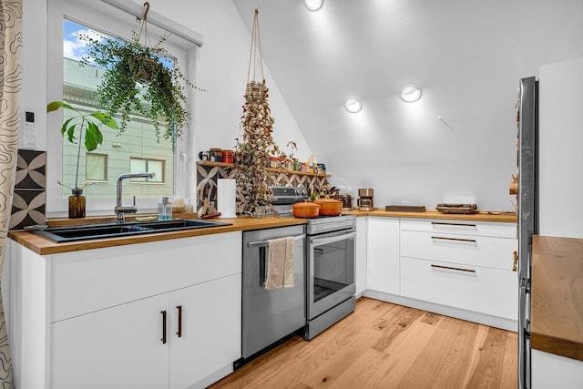 kitchen featuring appliances with stainless steel finishes, light wood-type flooring, a sink, butcher block counters, and white cabinetry