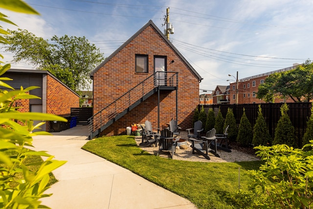 rear view of house featuring brick siding, a fire pit, fence, and a lawn