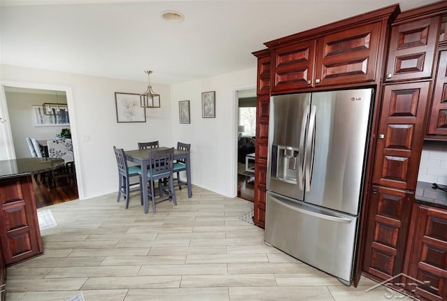 kitchen with dark countertops, an inviting chandelier, stainless steel fridge with ice dispenser, light wood-style flooring, and reddish brown cabinets