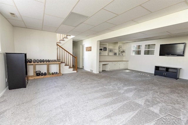 unfurnished living room featuring carpet flooring, stairs, a paneled ceiling, and visible vents
