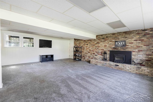 unfurnished living room with a wood stove, carpet flooring, and a paneled ceiling