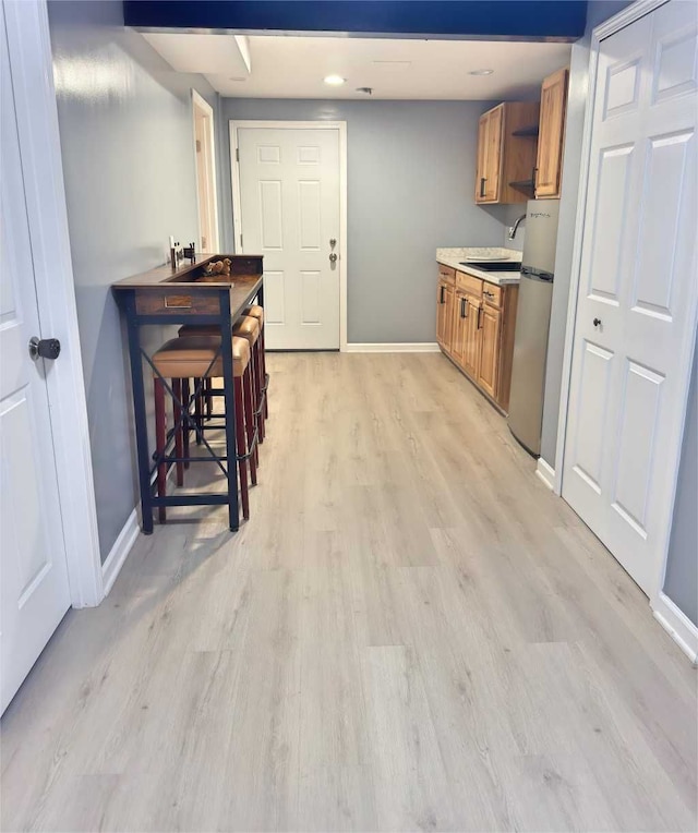 kitchen with brown cabinets, a sink, baseboards, freestanding refrigerator, and light wood-style floors