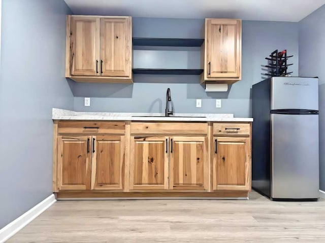 kitchen featuring a sink, light countertops, freestanding refrigerator, baseboards, and light wood-type flooring