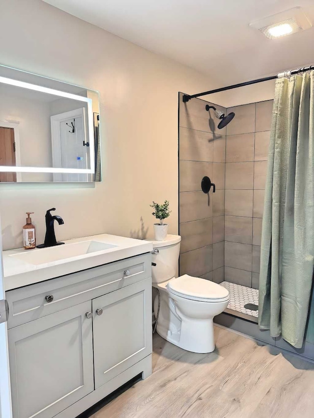 full bathroom featuring vanity, a tile shower, toilet, and wood finished floors