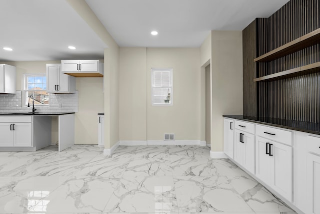 kitchen featuring dark countertops, tasteful backsplash, open shelves, a sink, and baseboards