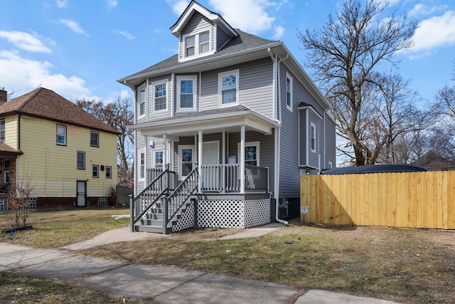 american foursquare style home featuring a front lawn, roof with shingles, fence, and covered porch