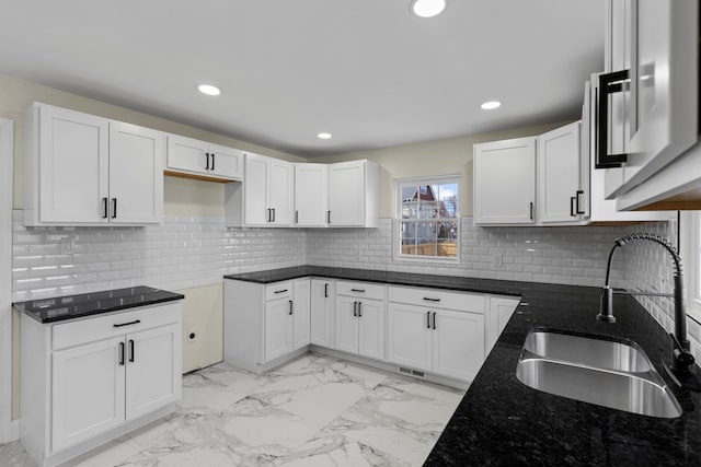 kitchen with a sink, marble finish floor, dark stone counters, white cabinetry, and decorative backsplash