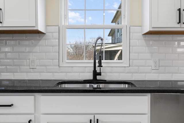 kitchen featuring a sink, decorative backsplash, white cabinets, and dark stone countertops